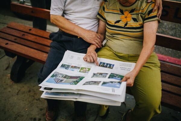 couple sitting on a bench, looking at a newspaper